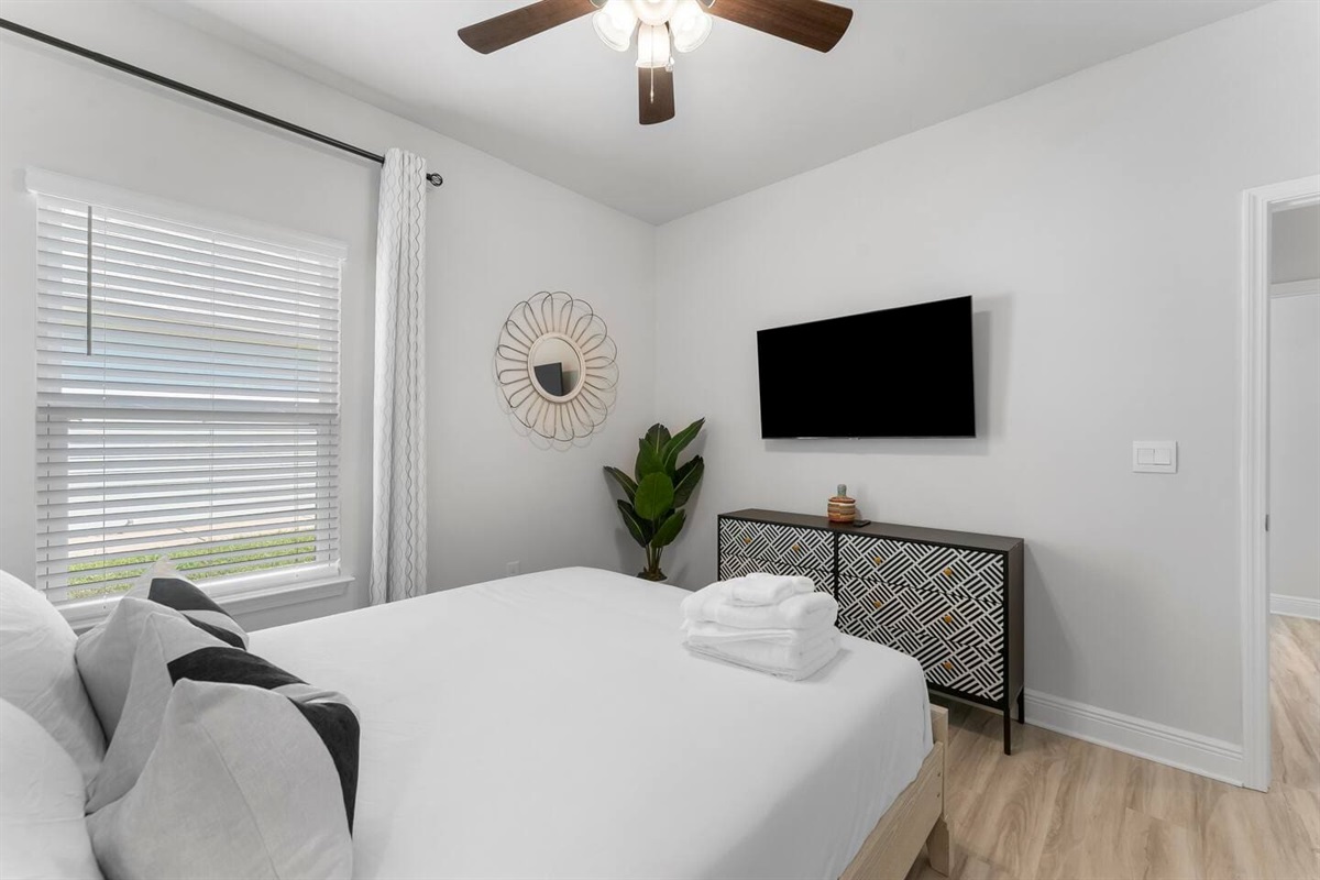 Spacious bedroom offering a flat-screen TV, ceiling fan, and functional bedside tables.