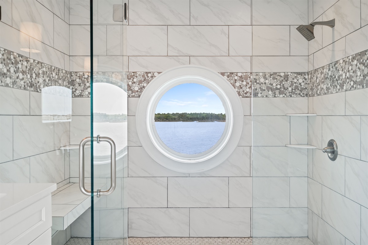 Unique walk-in shower with elegant tilework and a stunning porthole window overlooking the water