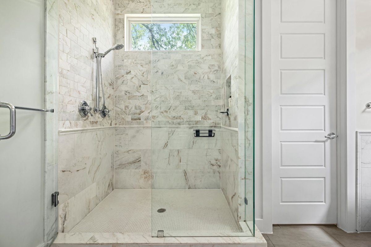 Frameless glass walk-in shower with marble tile surround and natural light — sleek, modern.