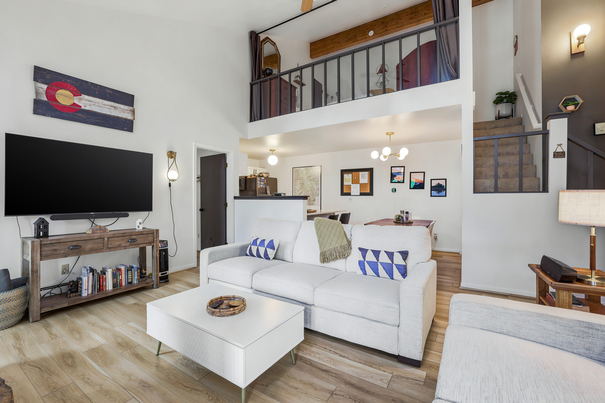 Living room with 65" TV and kitchen, dining area and loft in background