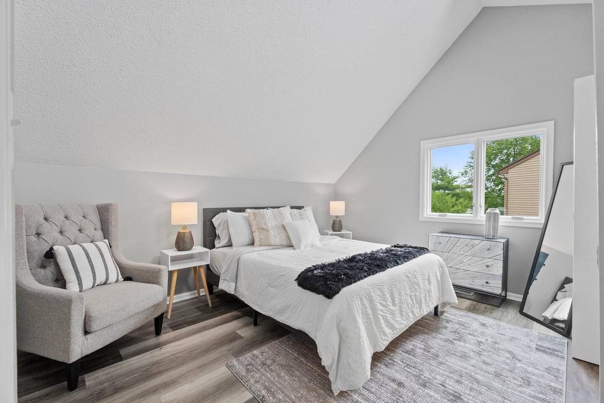 Sophisticated queen-sized bedroom, filled with natural light from a large window, complemented by a cozy side single sofa for extra comfort and relaxation.