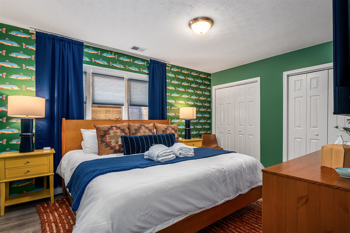 A charming, nature-inspired bedroom with playful trout wallpaper and cozy, layered bedding