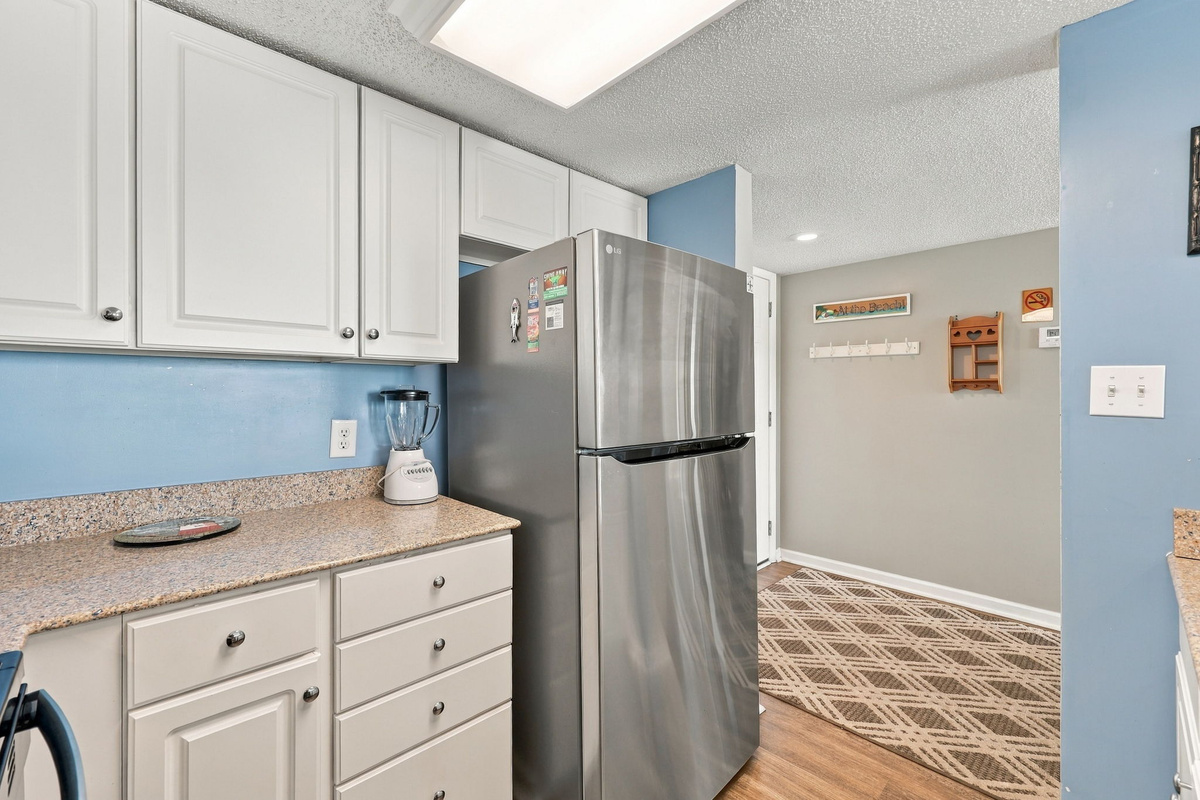 Close-up view of the kitchen area highlighting white cabinetry, granite countertops, and a modern stainless steel refrigerator.
