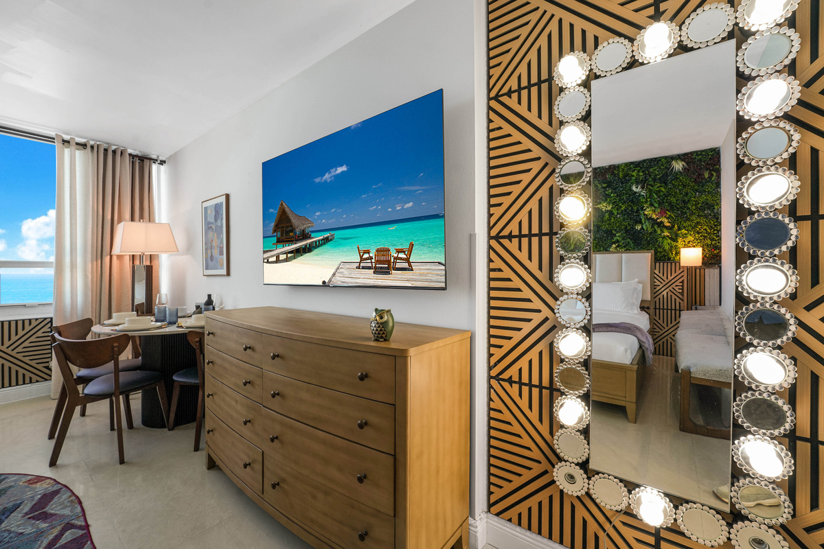 A six-foot illuminated floor mirror and natural pine dresser create a bright, hotel-style getting-ready corner beneath the 65-inch Smart TV.