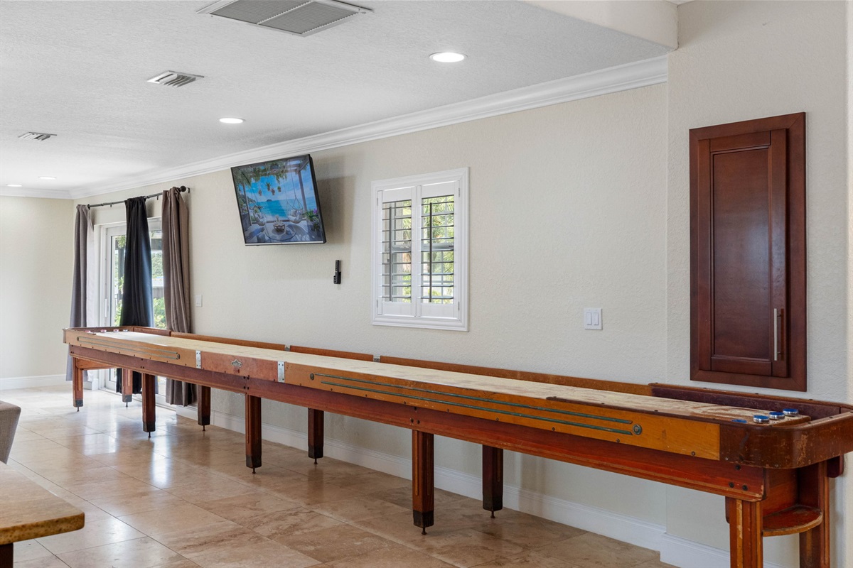 A full-length shuffleboard table lines the wall beneath a mounted flat-screen TV, perfect for game nights.