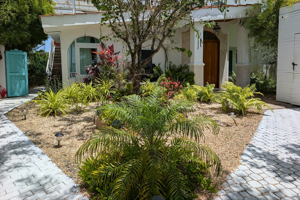Wide shot of the tropical entry courtyard at Villa Coral featuring stone paver walkways, a palm tree garden, grand pillars, and a custom wood front entry door in Dorado, Puerto Rico.

