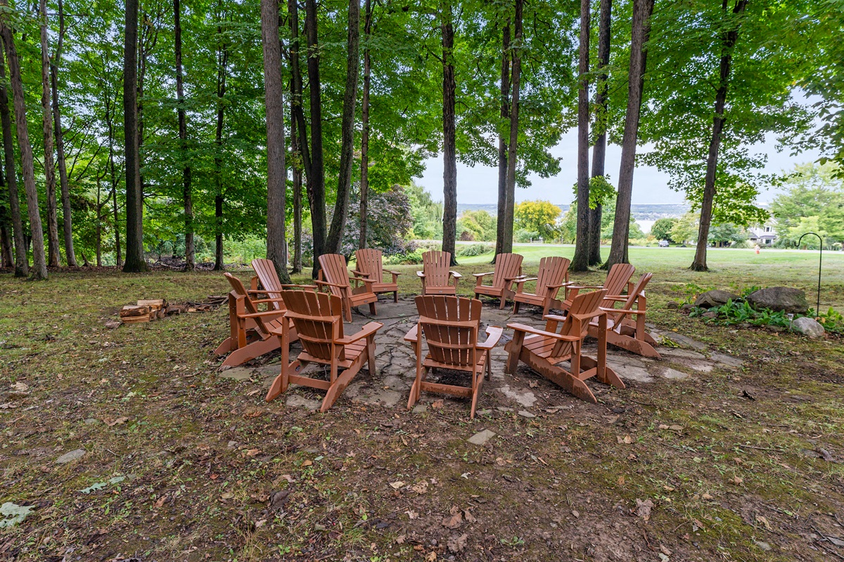 Gather around the fire pit under towering trees, complete with Adirondack chairs and a serene view of the lake in the distance.