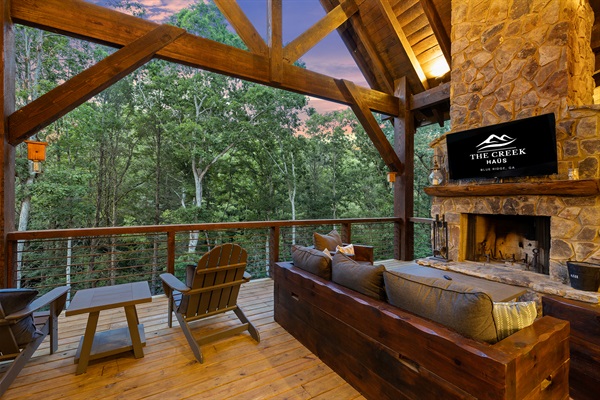Relax on the covered deck by the stunning stone fireplace, complete with plush seating and views of the surrounding woods.