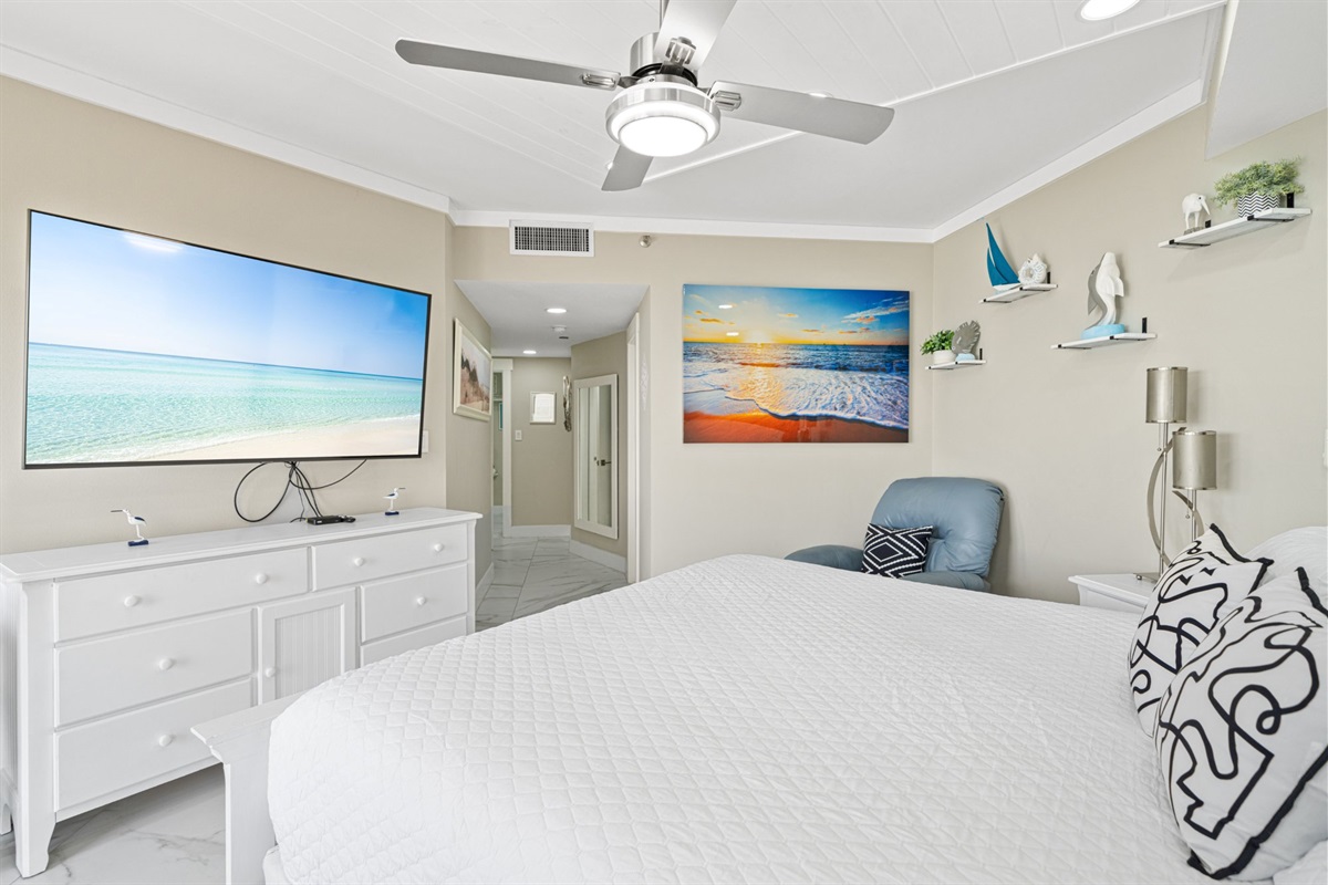 Coastal artwork, a leather recliner, a king bed dressed in crisp white linens, and a flat screen that fills the wall. This master suite is the kind of room that makes a week feel too short.