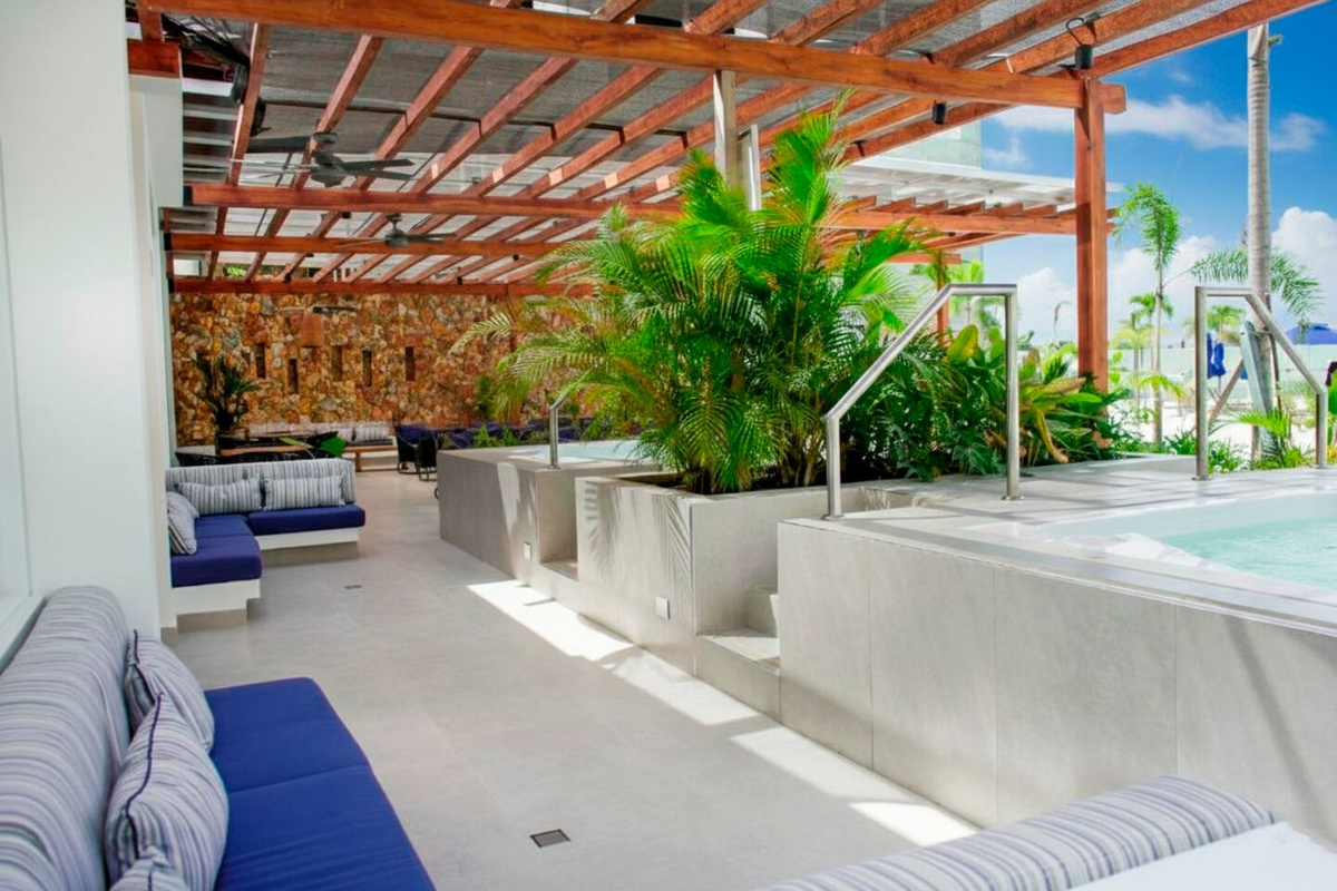 Gran piscina estilo laguna con tumbonas a la sombra, zonas de arena, áreas de descanso y acceso al spa, ofreciendo a los huéspedes mucho espacio para relajarse al aire libre.