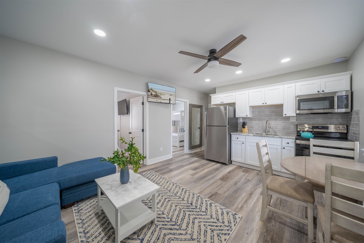 Open-plan living space combining the kitchen, dining, and seating areas. Bright lighting, modern appliances, and comfortable furnishings create an easy, functional layout suited for relaxing, dining, and moving through the space comfortably.