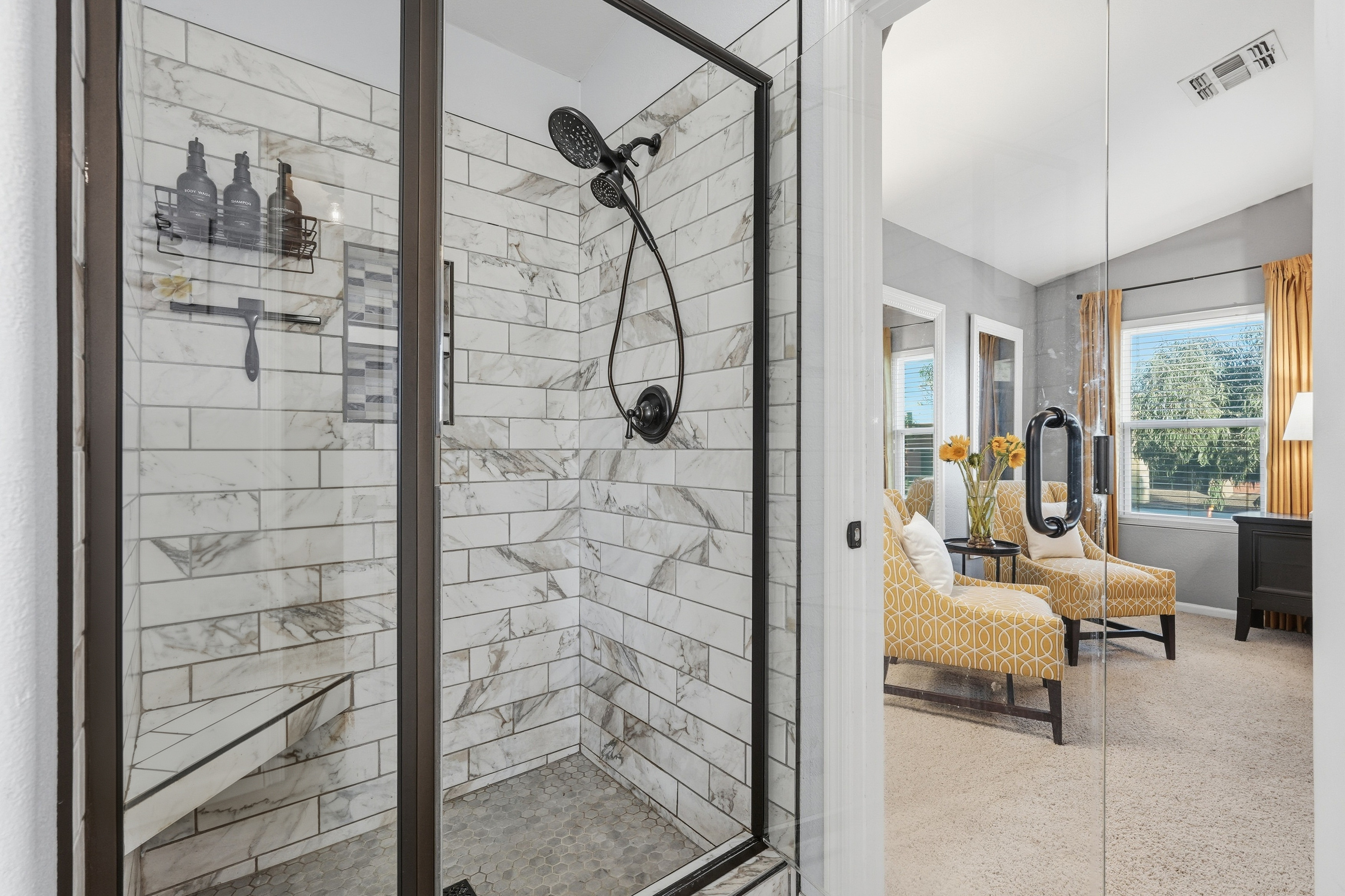 Master bathroom featuring a spacious glass-enclosed walk-in shower with marble-look tile, built-in bench, and easy access to the primary bedroom suite.