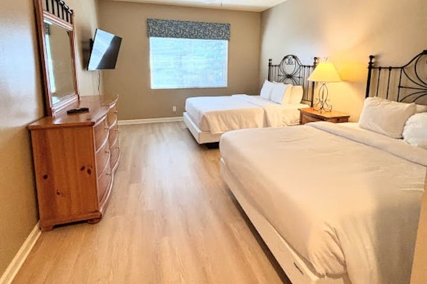 Comfortable bedroom with two beds, wood-look flooring, dresser storage, and a wall-mounted TV.