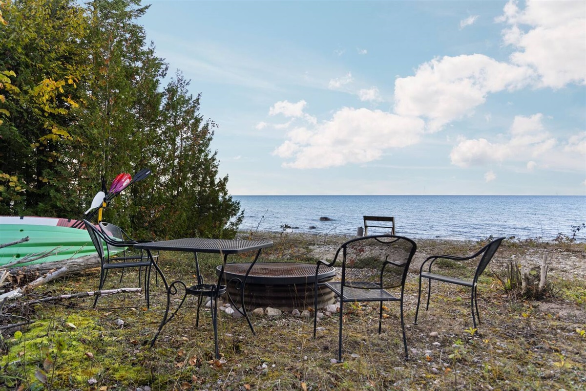 Lower campfire area with large firepit, table, and chairs.  The two provided kayaks and one paddleboard are stored in this area also.