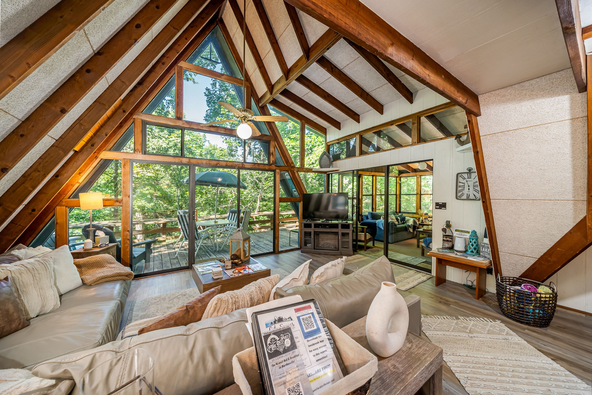Step into the main room and the A-frame ceiling opens up — vaulted beams overhead, deck just outside, and the whole space exhales with you.