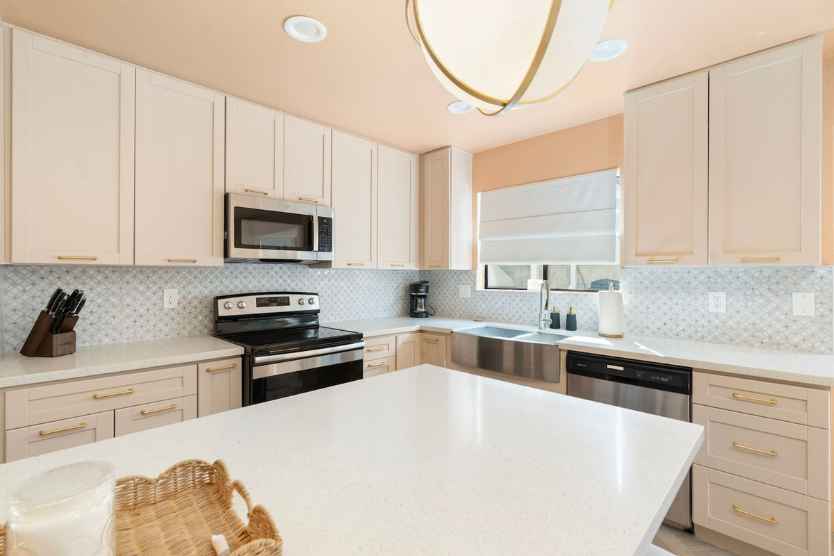 Kitchen with light wood cabinetry, quartz island, stainless appliances, and geometric backsplash—ready for home cooking.
