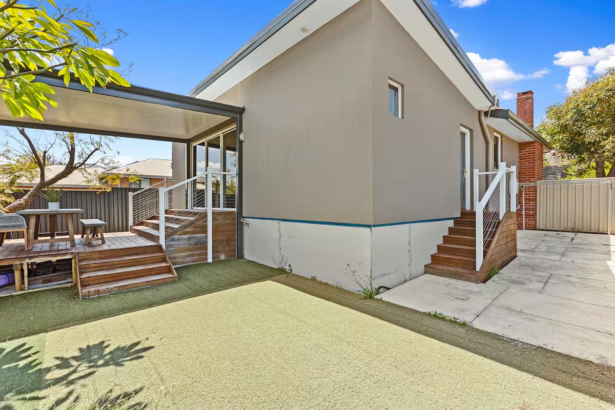 The backyard connects the covered deck, side entry and open paved area, adding useful outdoor space to Sasha’s Cottage on the Hill.