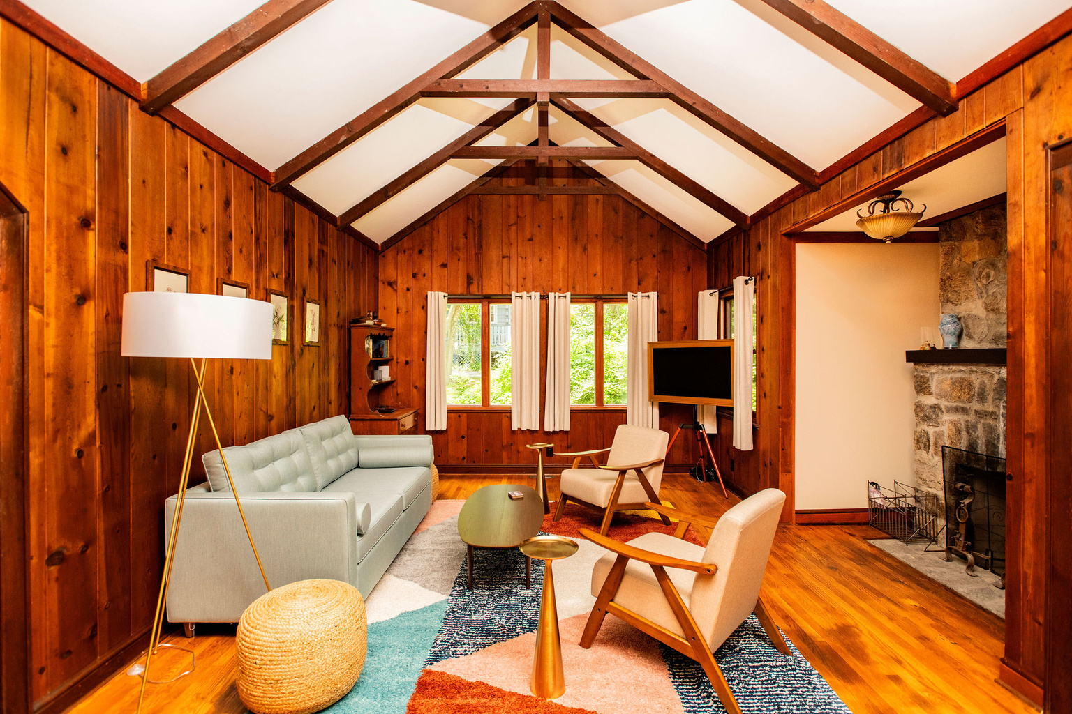 Light-filled living room with vaulted beamed ceilings, knotty pine walls and a stone fireplace