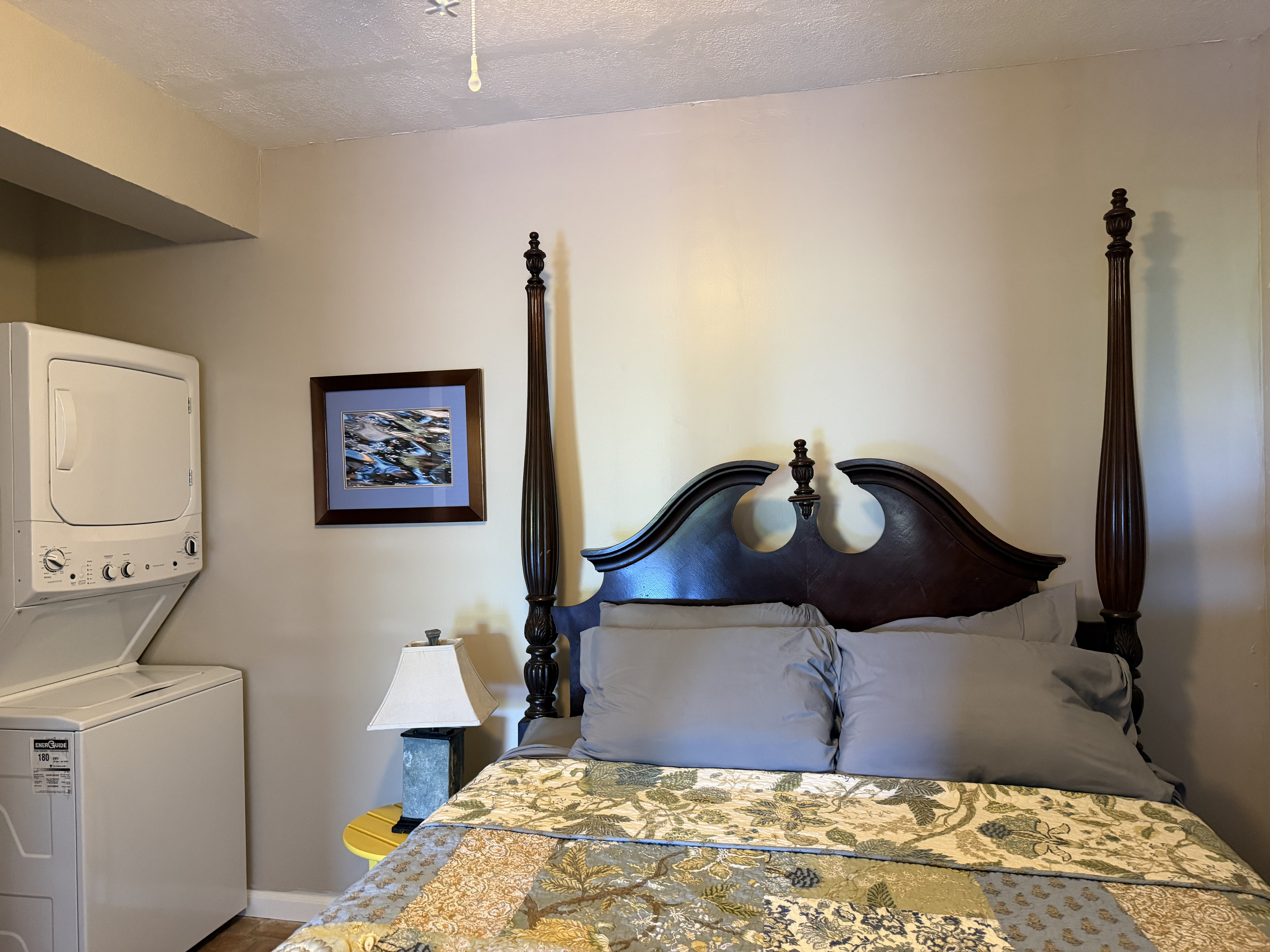 This comfortable apartment bedroom combines traditional style with tropical charm. The highlight is an elegant carved four-poster bed. Guests will also enjoy the ultimate convenience of having a stacked washer and dryer right inside the room.