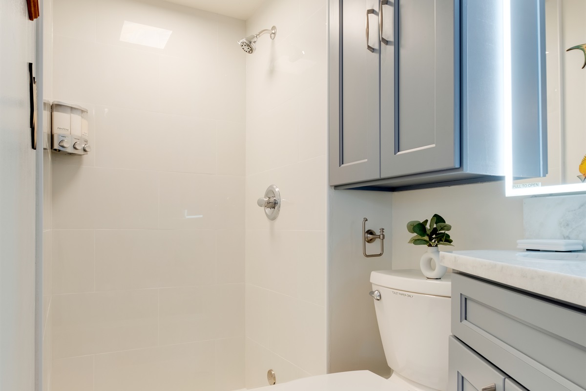 Refresh and rejuvenate in this bright, modern bathroom featuring sleek tile finishes and spa-inspired design. A perfect place to unwind after a day of Waikīkī sun and surf, offering both comfort and contemporary island style.