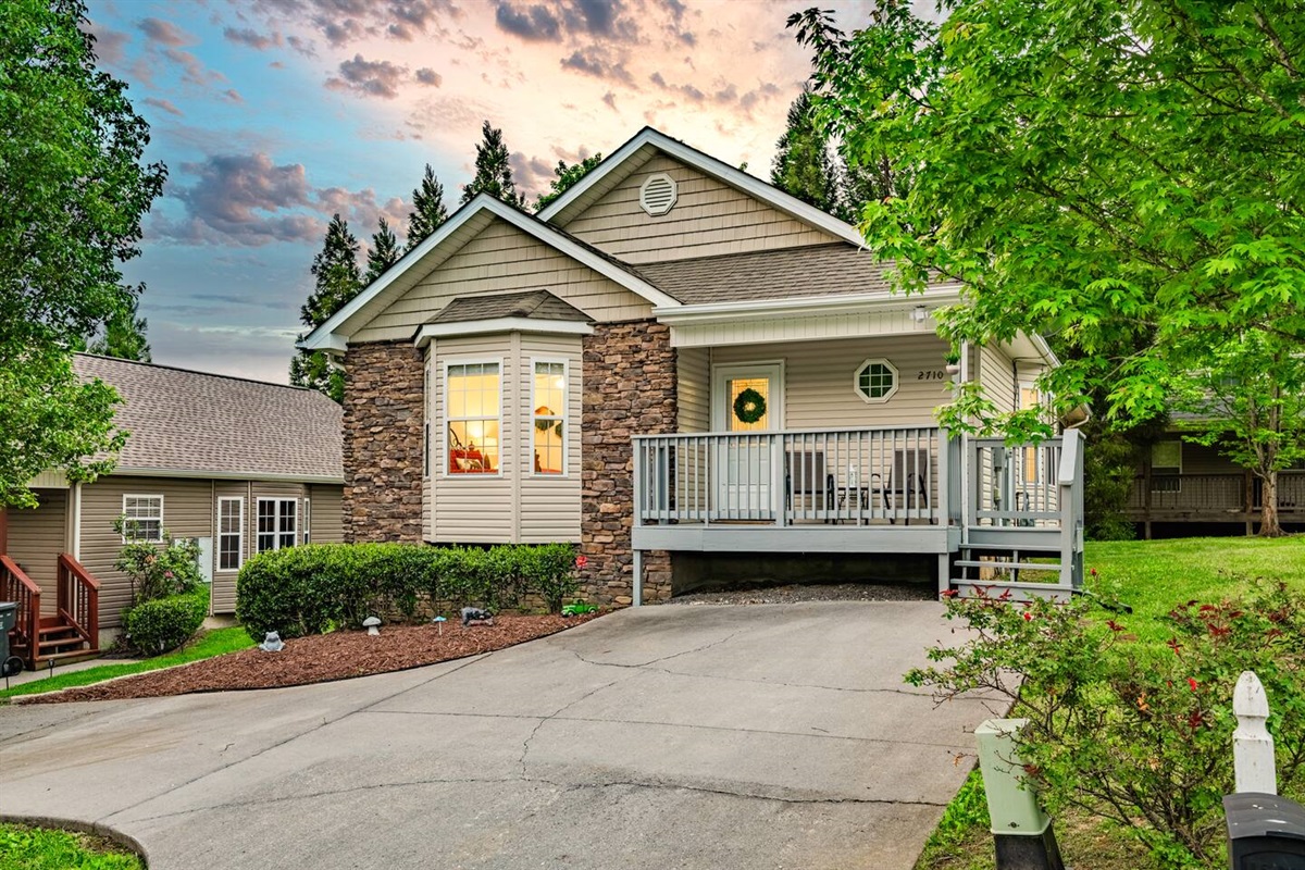 Beautiful stone-front home with a welcoming porch, private driveway, and lush greenery—an inviting retreat in a peaceful neighborhood.