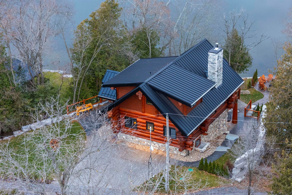 Aerial view of Bear Lodge showing lake access, wrap-around decking, firepit, and private wooded setting.