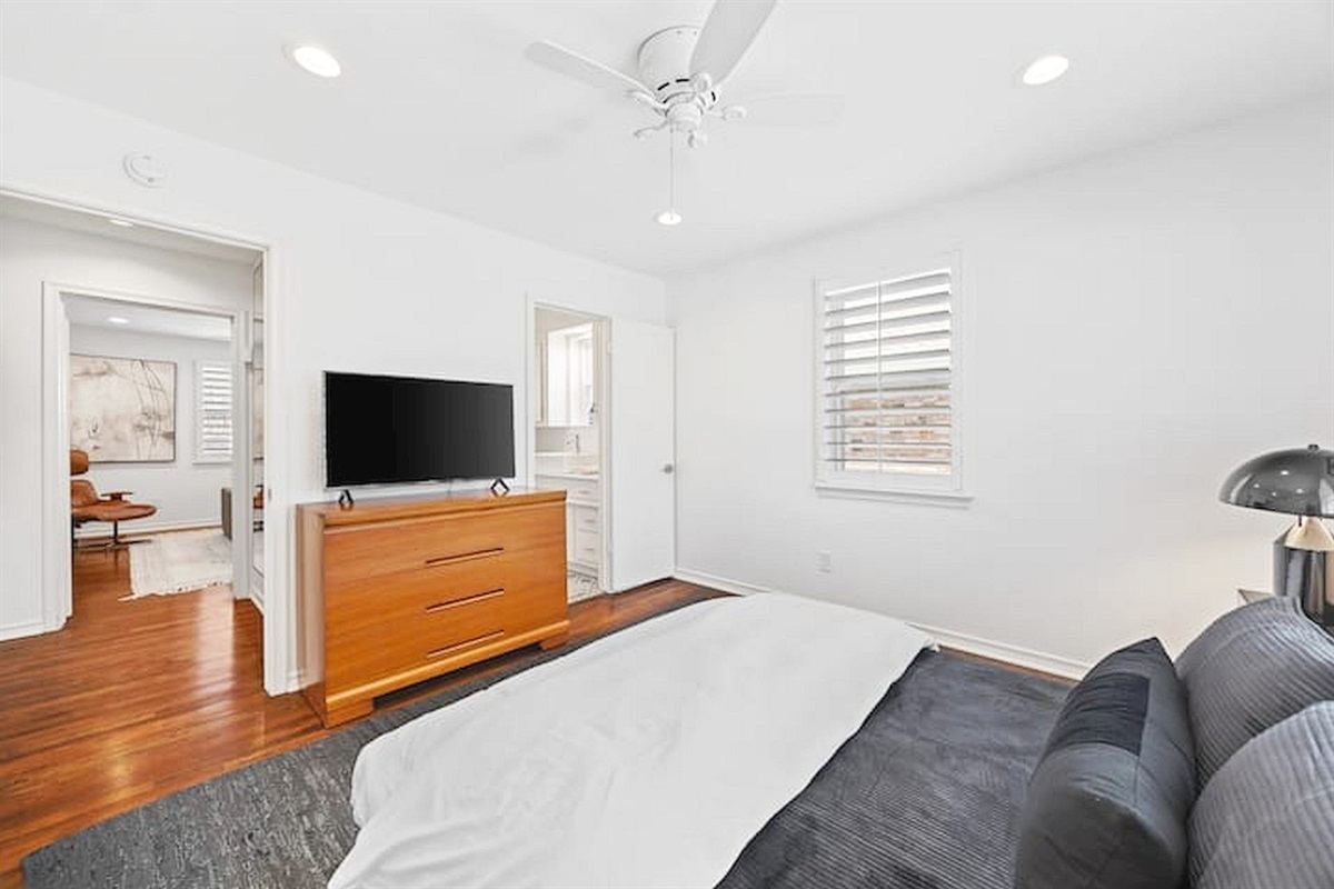 Relax in a serene primary suite featuring warm wood accents, a smart TV, ensuite bath access, and a calming atmosphere designed for restful stays.