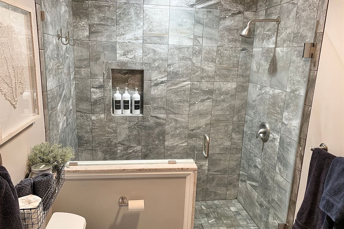 Step into this luxurious glass-enclosed shower, featuring floor-to-ceiling grey marble-style tile and a built-in niche for amenities. The modern fixtures and clean design provide a refreshing, spa-like experience after a day in the sand.