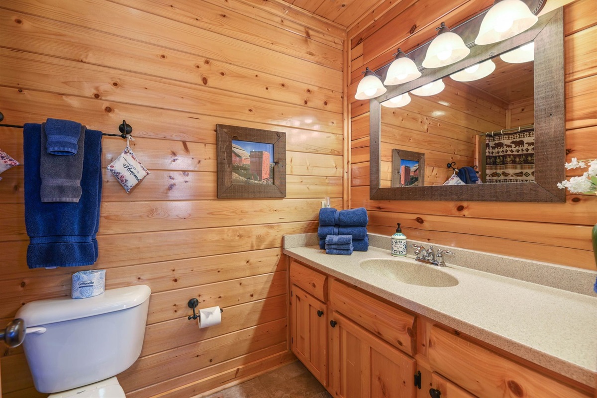 - Bright bathroom with rustic wood walls and soft cabin lighting throughout   - Spacious vanity and mirror add a touch of comfort and practicality   - Perfect balance of rustic style and modern convenience for your stay