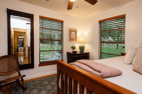 Bright corner windows overlooking yard with full-length mirror and rocking chair.