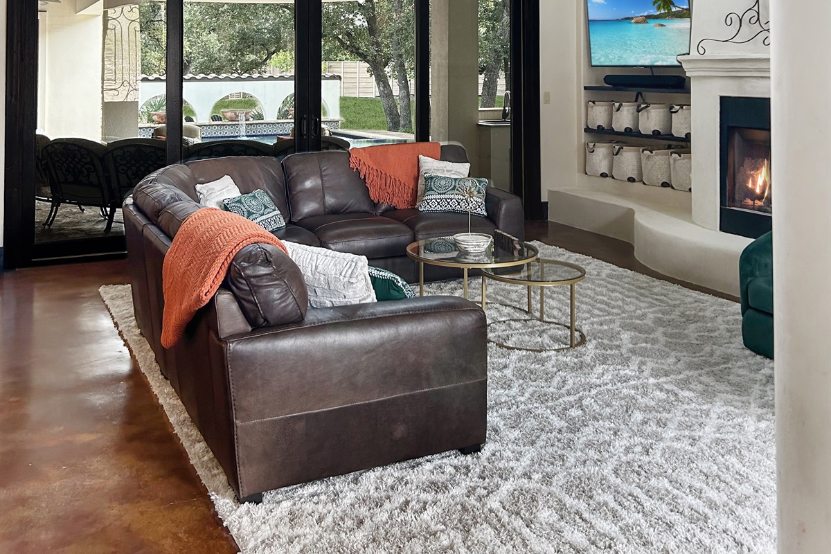 "Welcome to the heart of the house! This spacious living room boasts over 20-foot ceilings, abundant seating, a cozy fireplace, and a smart TV—all with stunning views of the resort-style pool.