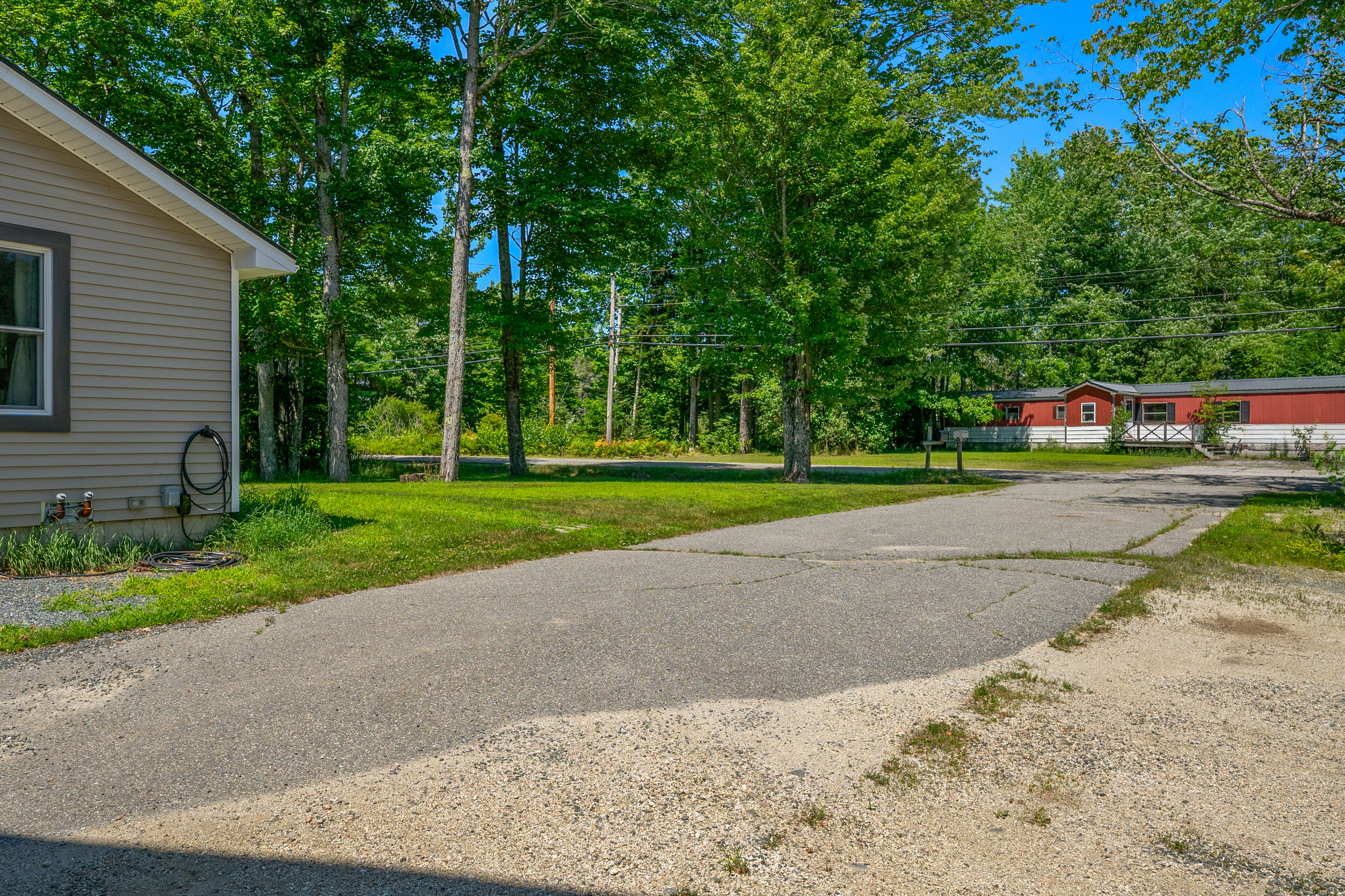 View back toward the road from the wide paved driveway, highlighting where the gravel loop begins. This seamless transition provides the pull-through path for large trailer rigs, boats, and ATVs to circle the home without backing up.