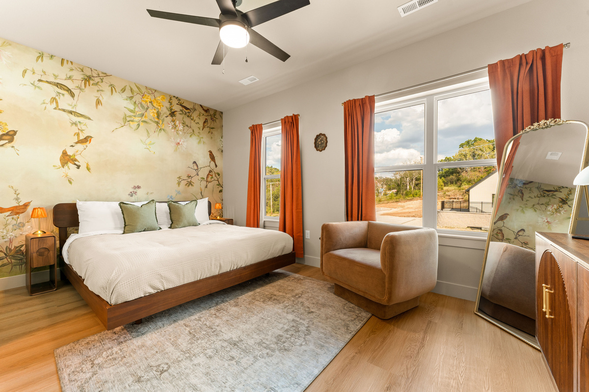 Wake up surrounded by whimsical details in this spacious king bedroom, featuring a beautiful bird-and-botanical mural, warm wood furnishings, and oversized windows filled with natural light.