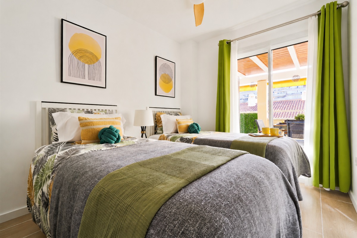 Bright and calming twin bedroom with tropical tones, soft linens, and direct access to the terrace — perfect for relaxed mornings and restful nights.