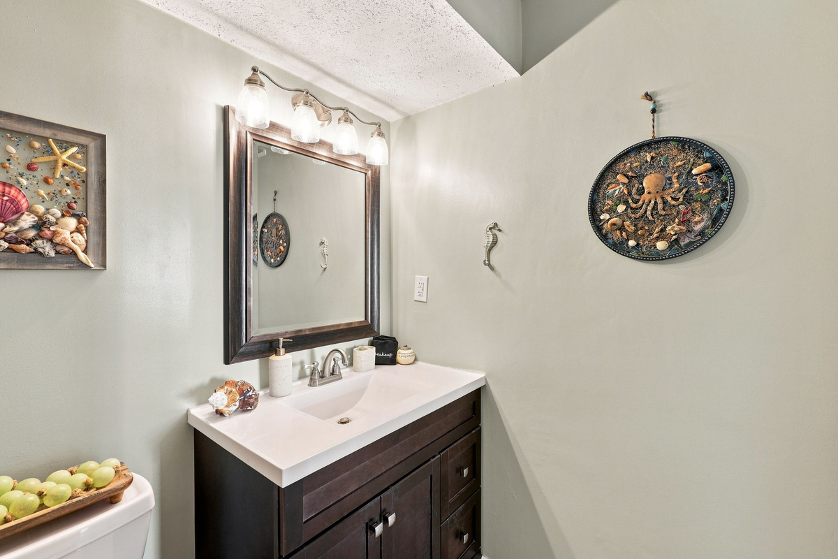 Clean and well-lit bathroom vanity featuring a rich wood finish, large mirror, and charming coastal wall decor.