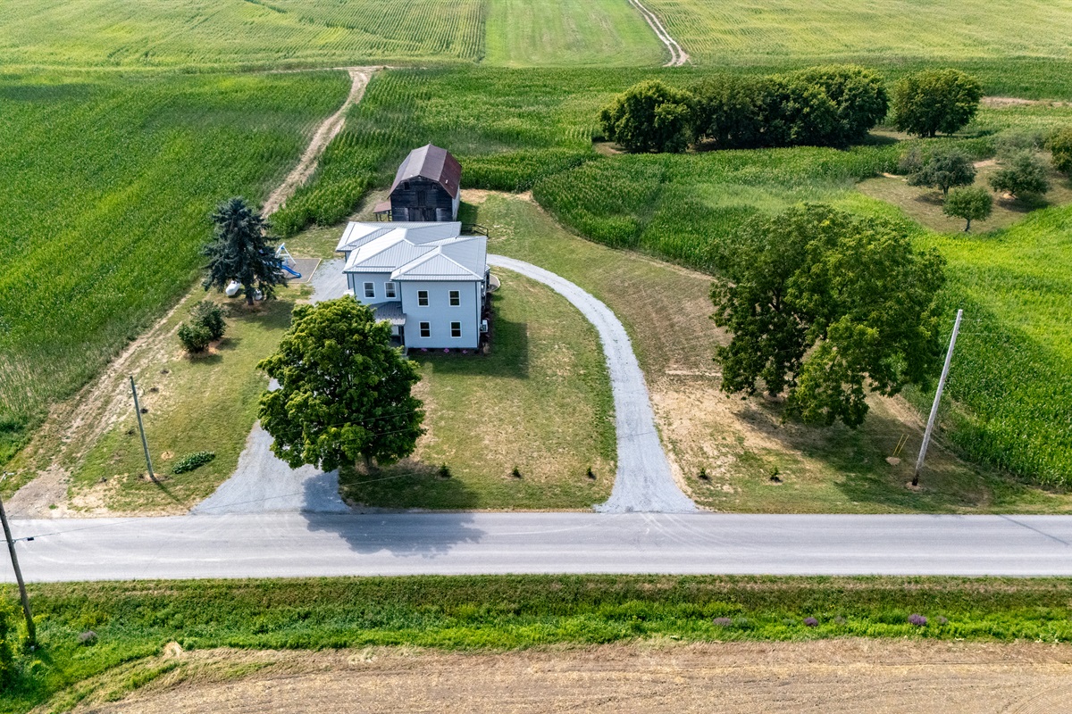 Scenic entryway with a winding drive leading to a spacious farmhouse oasis tucked among green fields.
