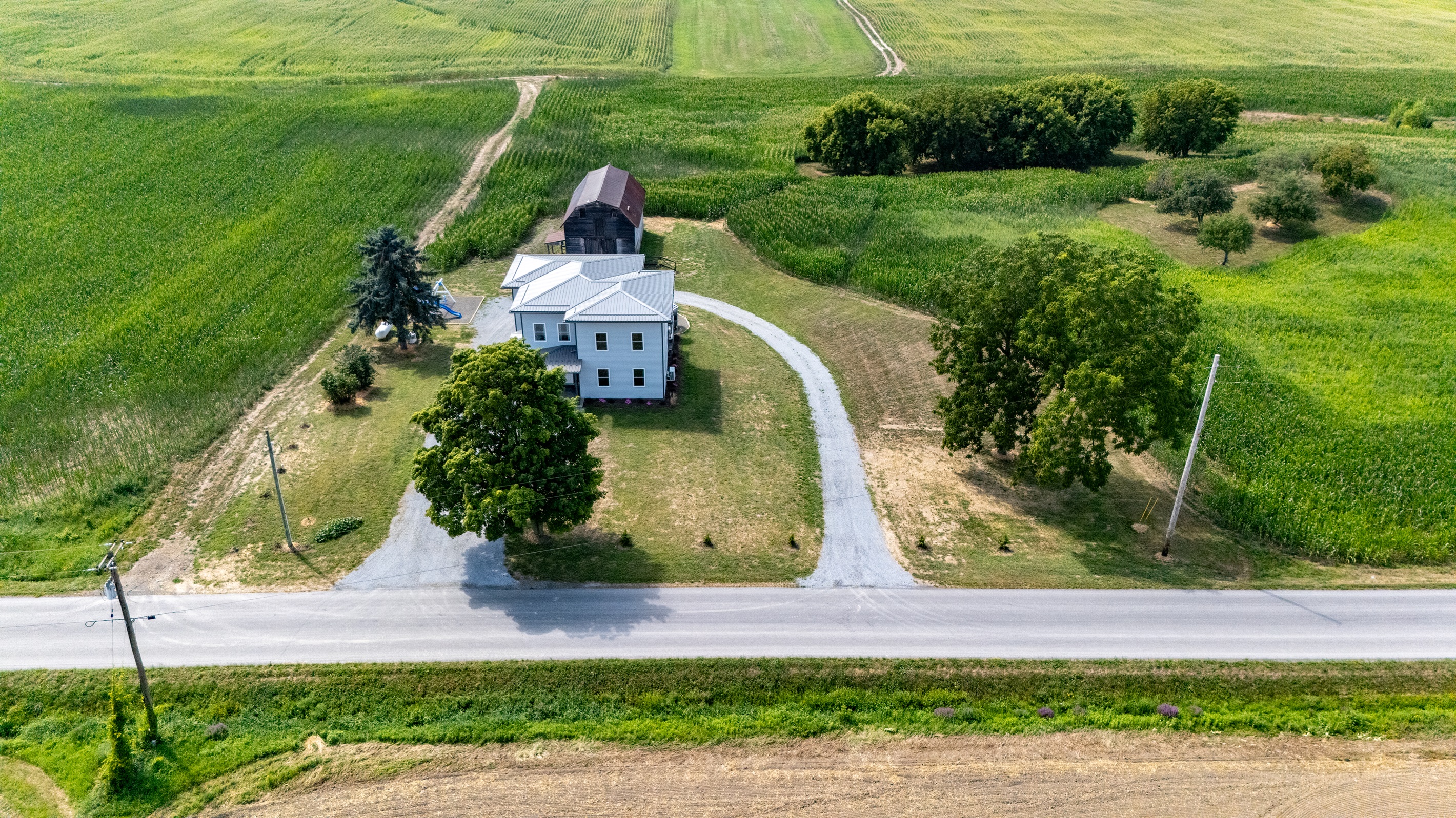 Scenic entryway with a winding drive leading to a spacious farmhouse oasis tucked among green fields.