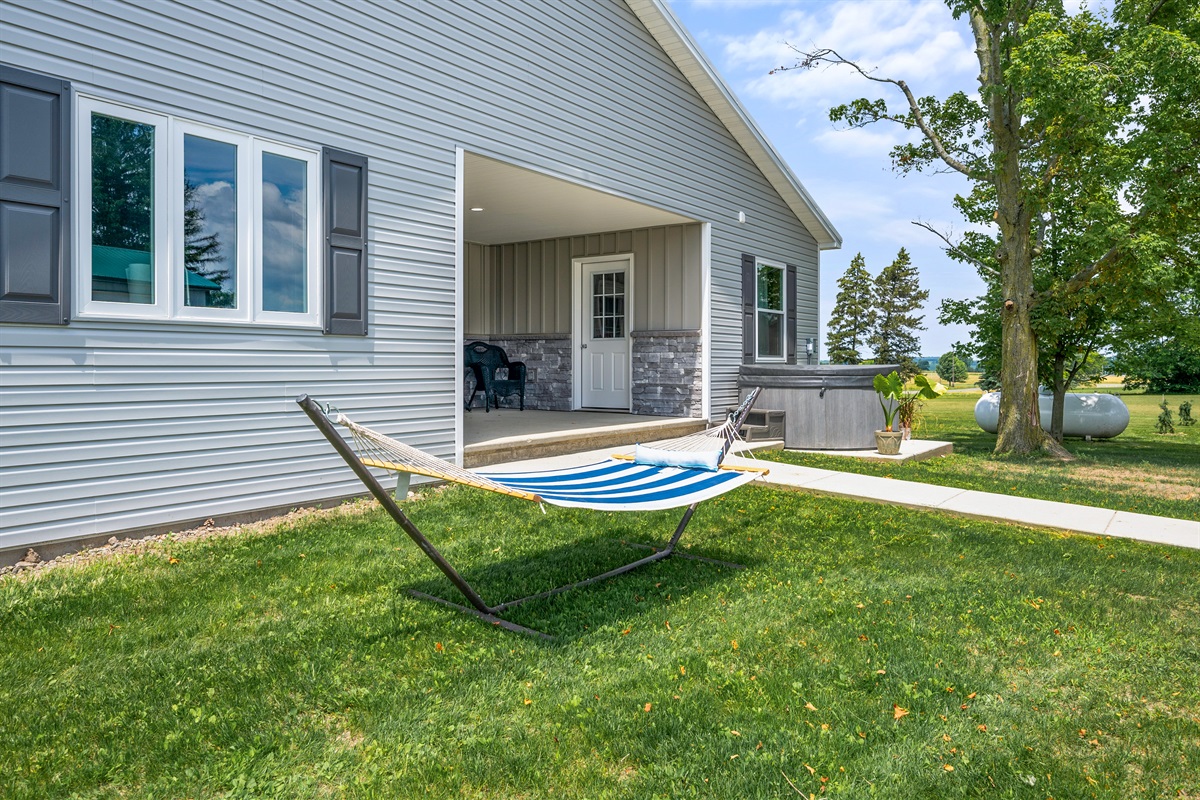 Relax and unwind in this peaceful backyard retreat featuring a cozy hammock, covered patio seating, and a private hot tub—perfect for soaking in the countryside charm.