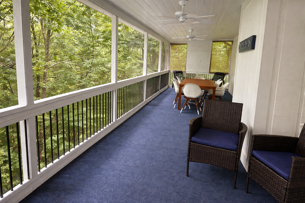 Large screened-in porch with dining area, ceiling fans, and peaceful wooded views.