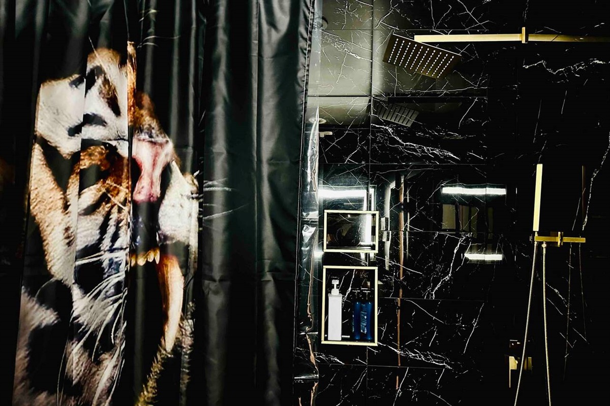This epic black bathroom also features black marble titles, gold fixtures, a tiger shower curtain.