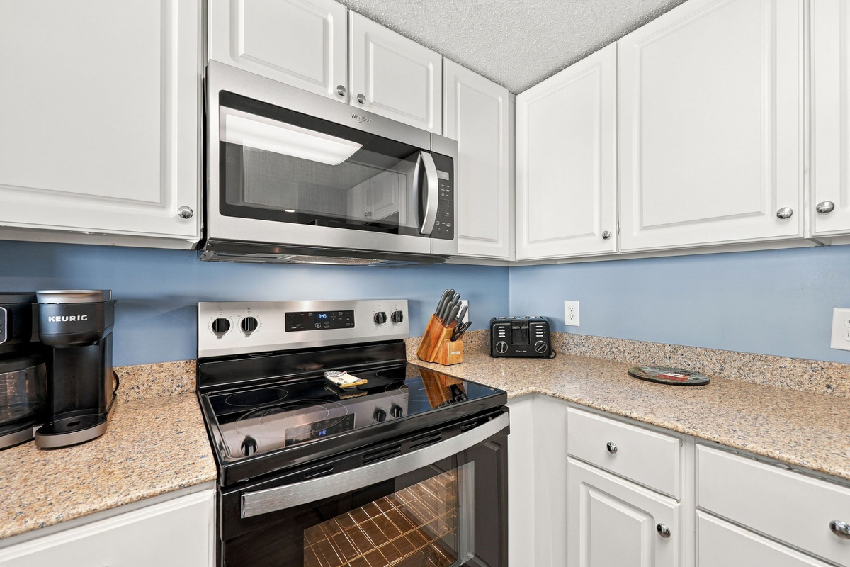 Kitchen view showcasing white cabinetry, granite countertops, a stainless steel microwave and stove, and a Keurig coffee maker.