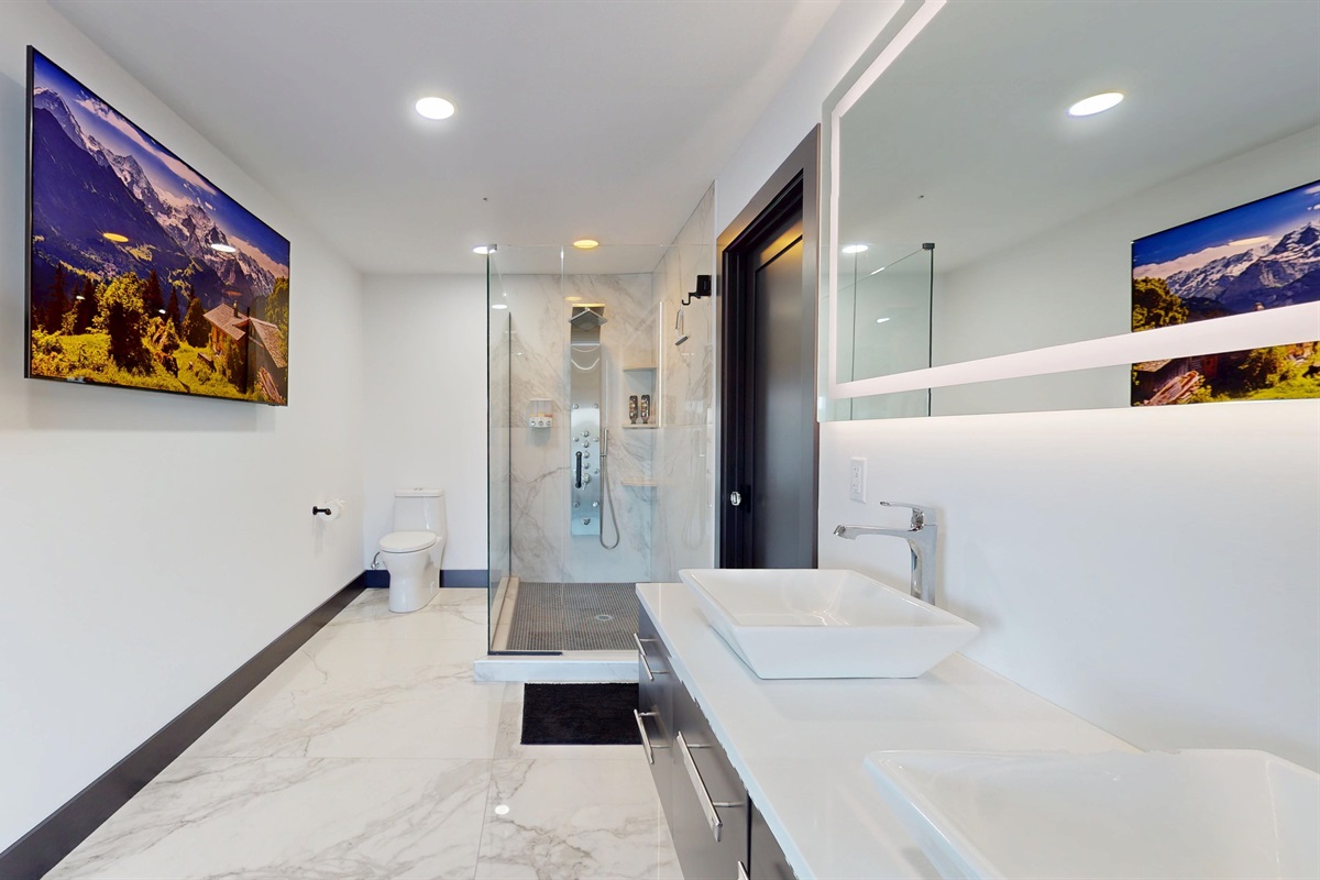Large open space full bathroom with double vanity, toilet, large walk-in shower with full body sprayer and rainhead, and a 85" SmartTV.