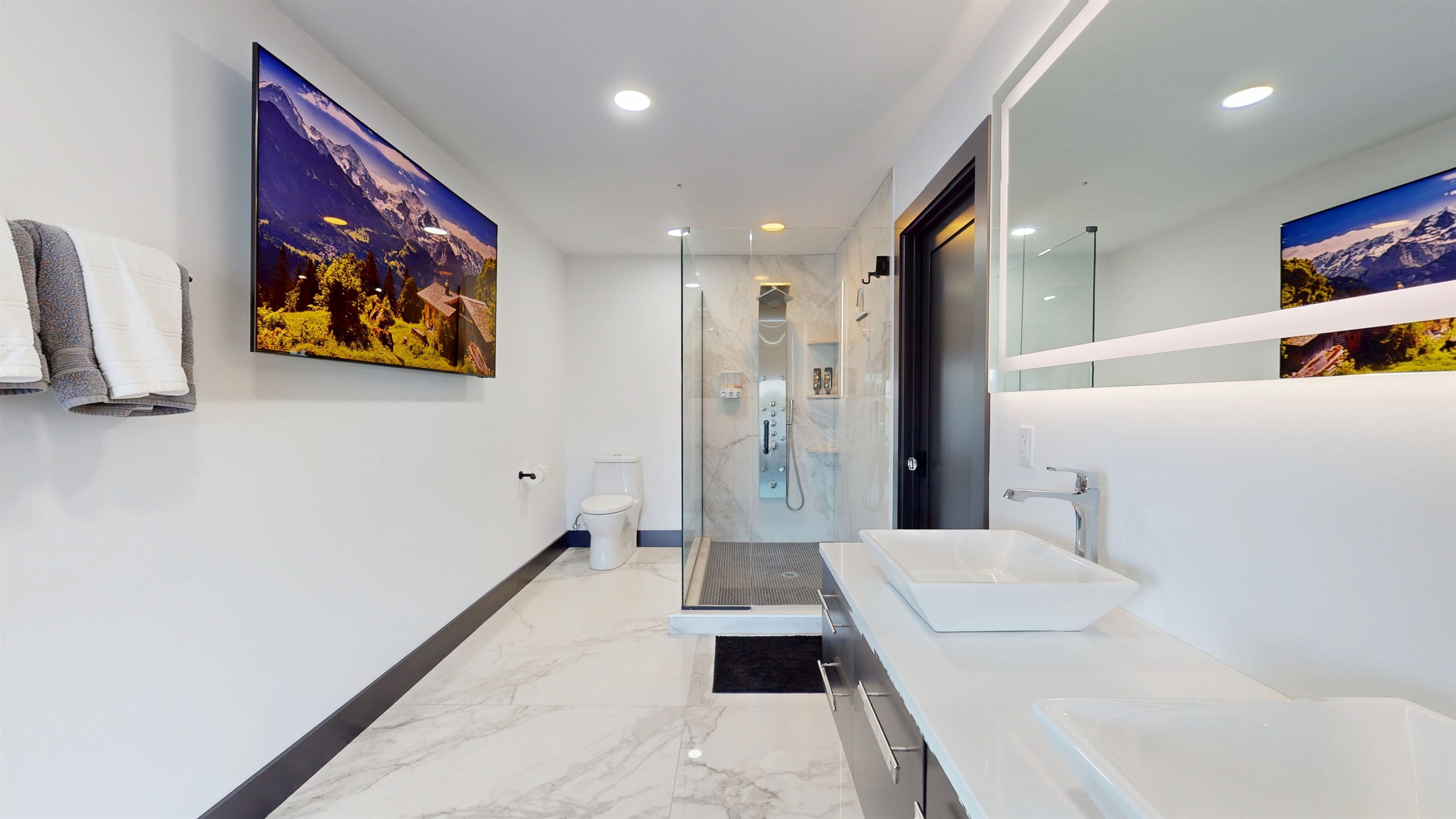Large open space full bathroom with double vanity, toilet, large walk-in shower with full body sprayer and rainhead, and a 85" SmartTV.