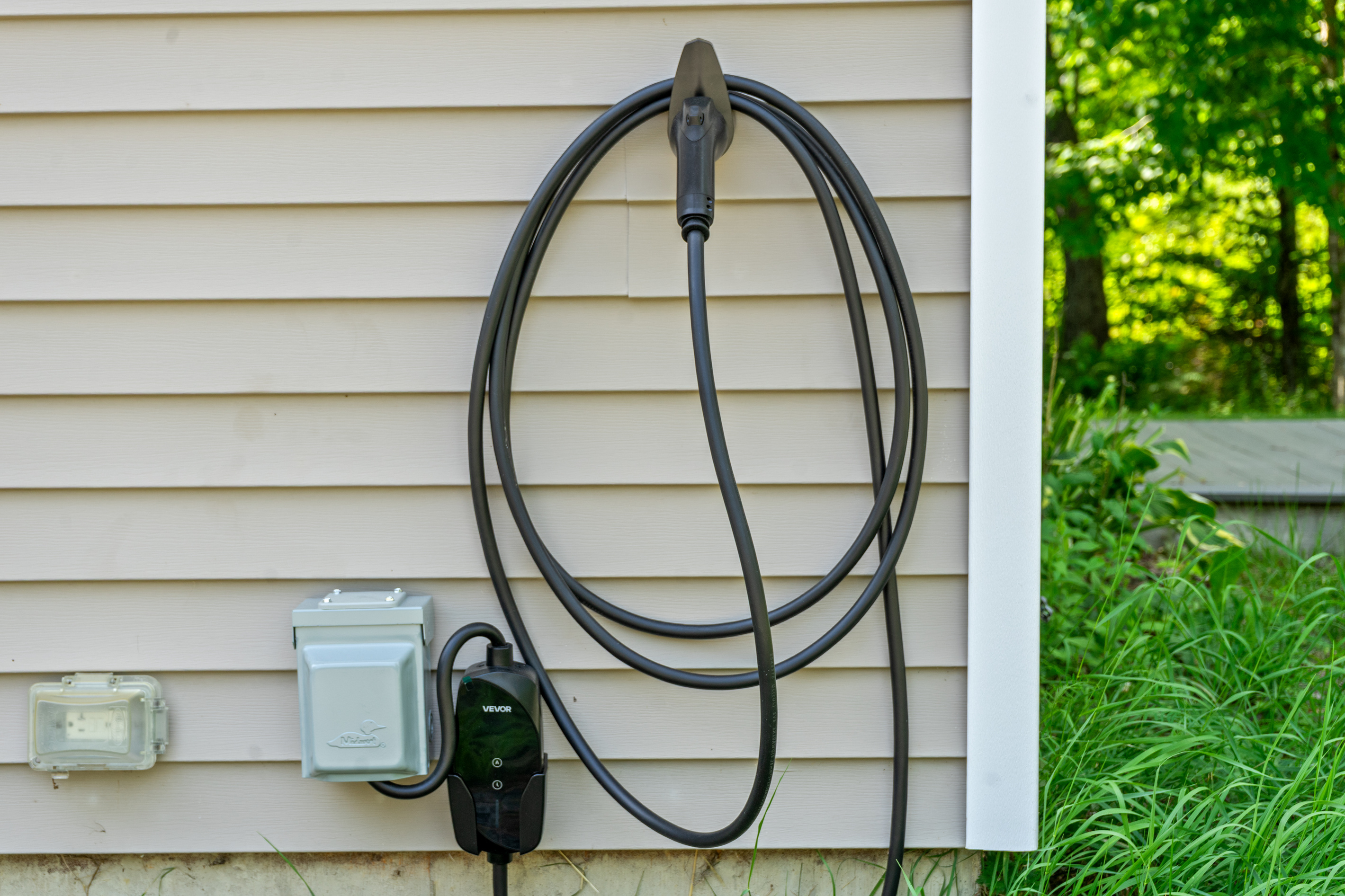 Utilize the dedicated Level 2 EV charging station with a universal VEVOR plug interface. Mounted directly on the home's exterior siding, this complimentary electric vehicle charger provides fast overnight charging for your car or SUV.