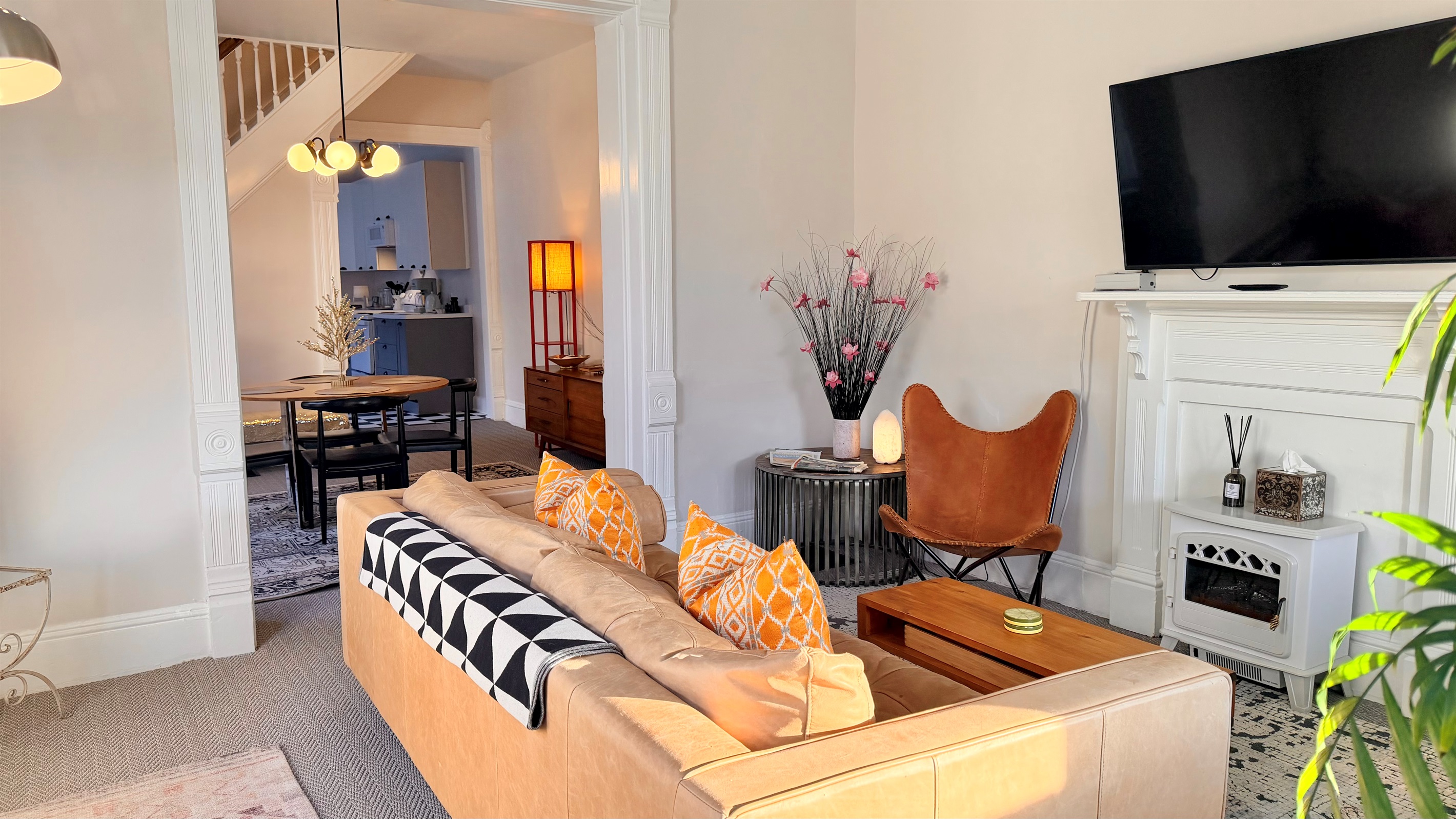 Living room with a leather sofa, two chairs, area rugs, lamps, and electric fireplace beneath a mounted TV. The front door opens into this room, which flows through the dining area, kitchen, laundry room and out the back door to the yard and parking.
