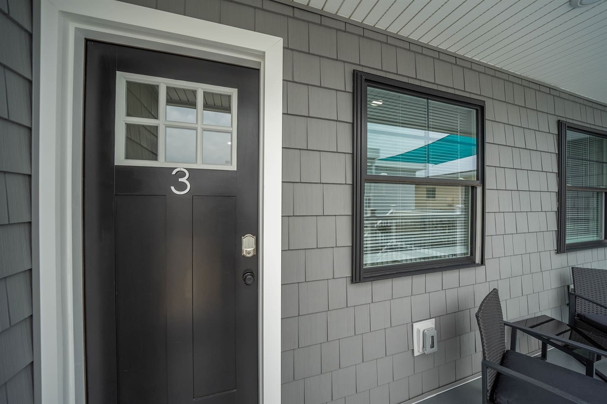 Private covered entry with clear unit numbering, secure keypad access, and sheltered walkway. Adjacent seating offers a convenient spot to pause or enjoy fresh air, creating a calm and easy arrival experience before stepping inside.