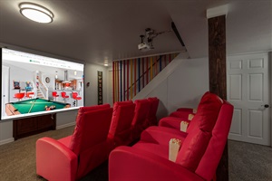Cozy theater room with red recliner seating, a large projector screen, and popcorn-ready setup, perfect for movie nights and relaxing with your group.
