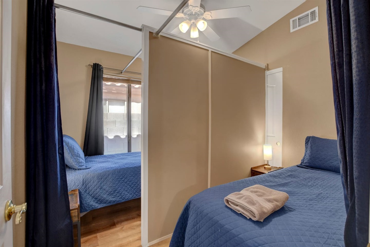 Cozy split bedroom with two comfy beds, ceiling fan, and warm natural light