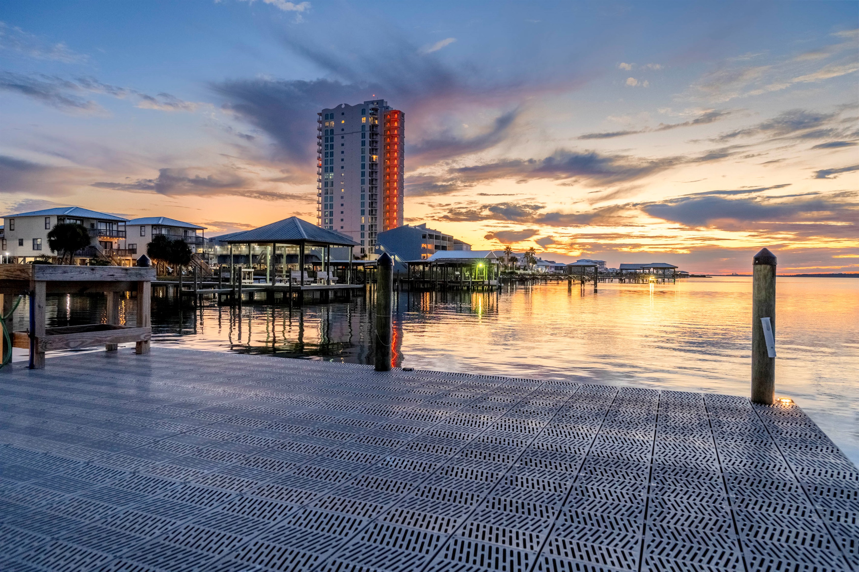 Tranquil waterfront sunset with modern buildings and glowing reflections.