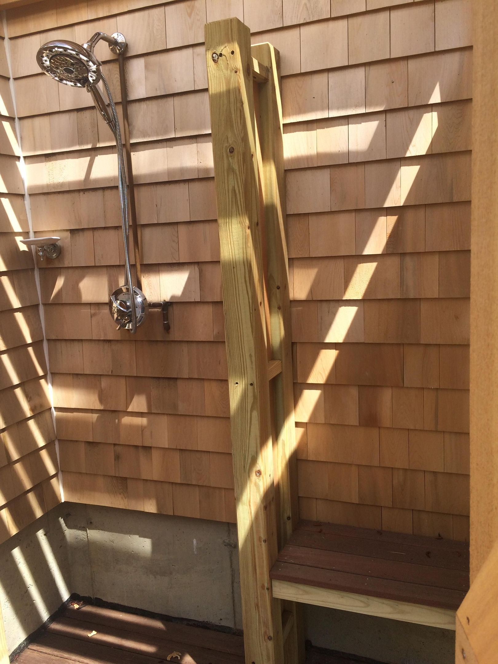 outside shower with rain shower head and dressing area with bench.